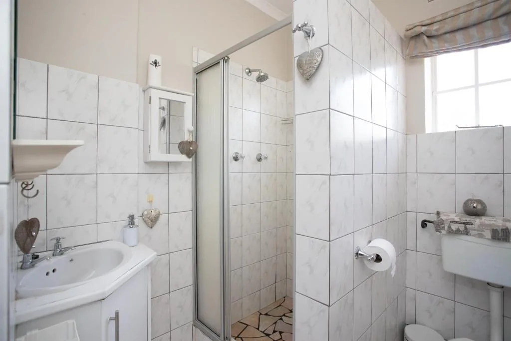 Bright white-tiled bathroom with curved sink, walk-in shower, and decorative heart accents