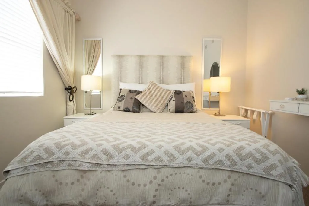 Neutral toned bedroom with queen bed, decorative pillows, bedside lamps