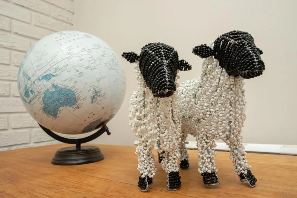 Decorative beaded sheep figurines and globe on wooden table