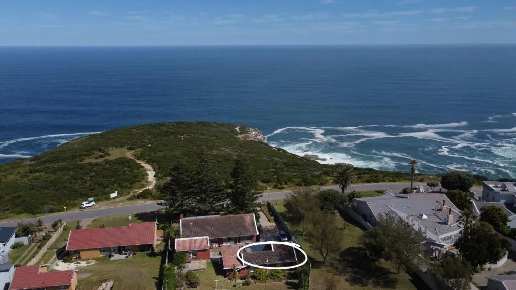 Aerial view of coastal property with ocean, cliffs, and surrounding gardens