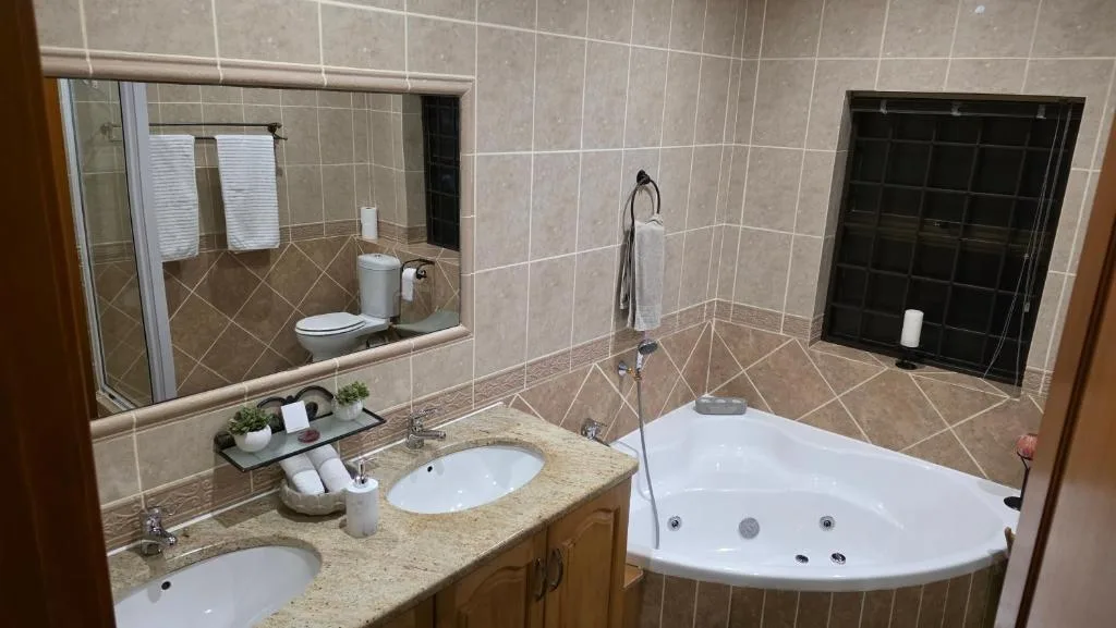 Spacious bathroom with double vanity, corner spa bath, and large mirror