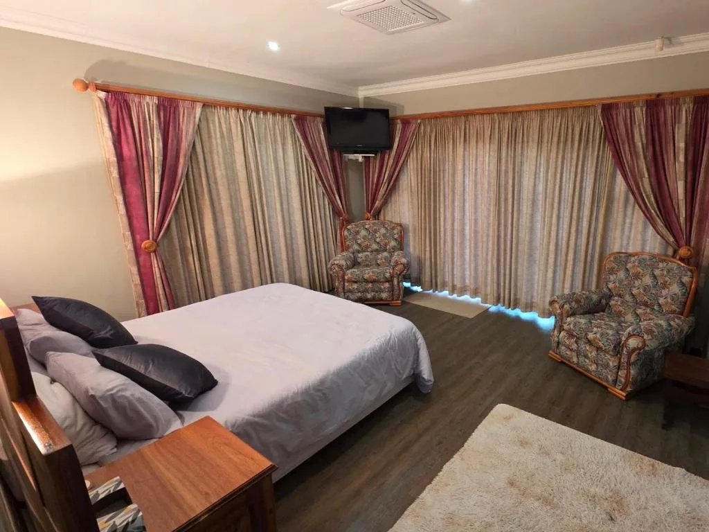 Spacious bedroom with queen bed, patterned armchairs, and burgundy curtains