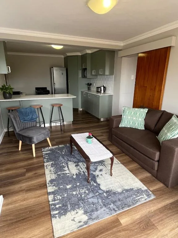 Open-plan lounge with brown sofa, armchair, coffee table, and kitchen beyond