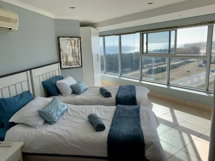 Bright bedroom with twin beds and expansive coastal views through large windows