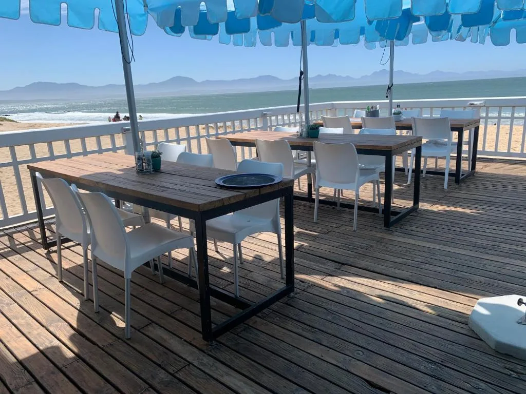 Seaside deck with dining tables, white chairs, blue umbrellas, ocean view
