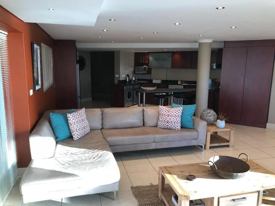 Modern lounge with gray sofa, colorful pillows, and open kitchen beyond