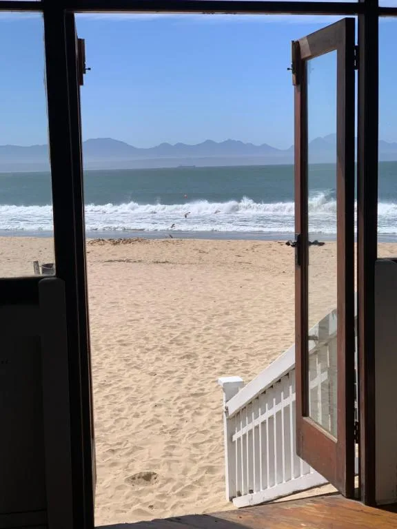 Ocean waves and sandy beach viewed through open glass doors from indoors