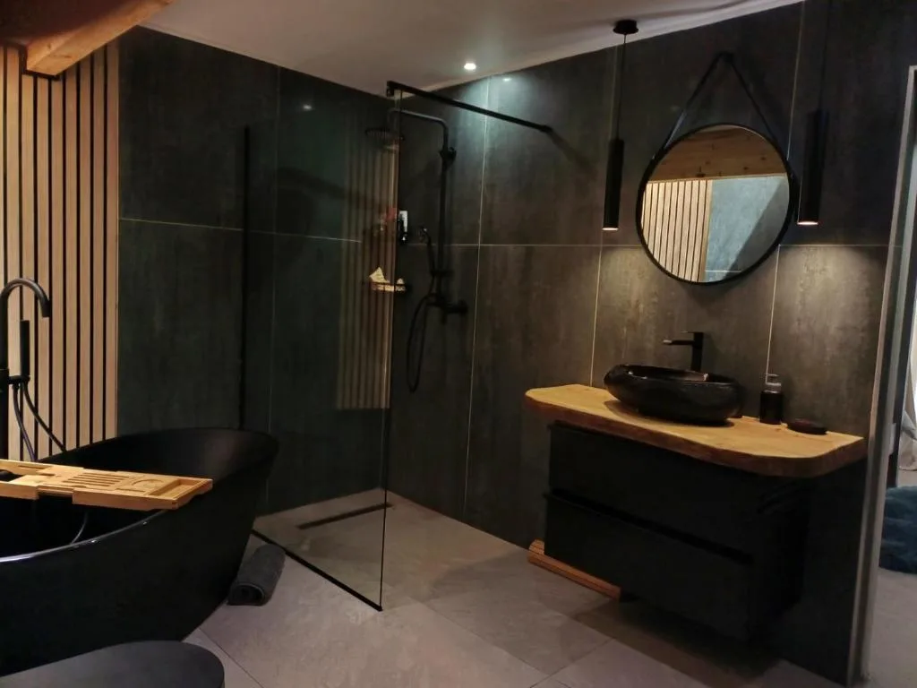 Modern bathroom with black freestanding tub, glass shower enclosure, wooden vanity