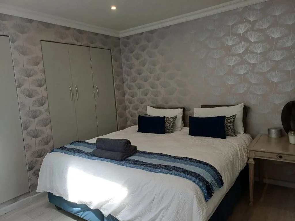 Spacious bedroom with queen bed, elegant wallpaper, wardrobe, and bedside table
