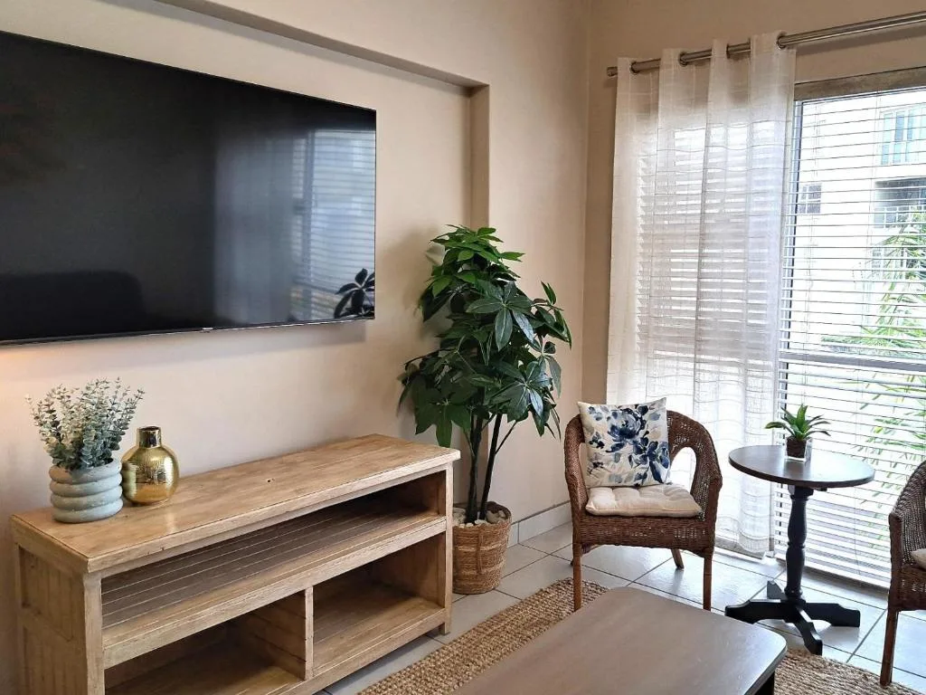 Bright lounge with TV, wooden furniture, plants, and garden views