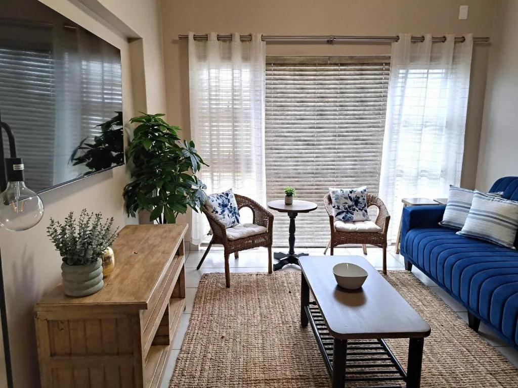 Bright living room with blue sofa, wicker chairs, and garden views through shutters