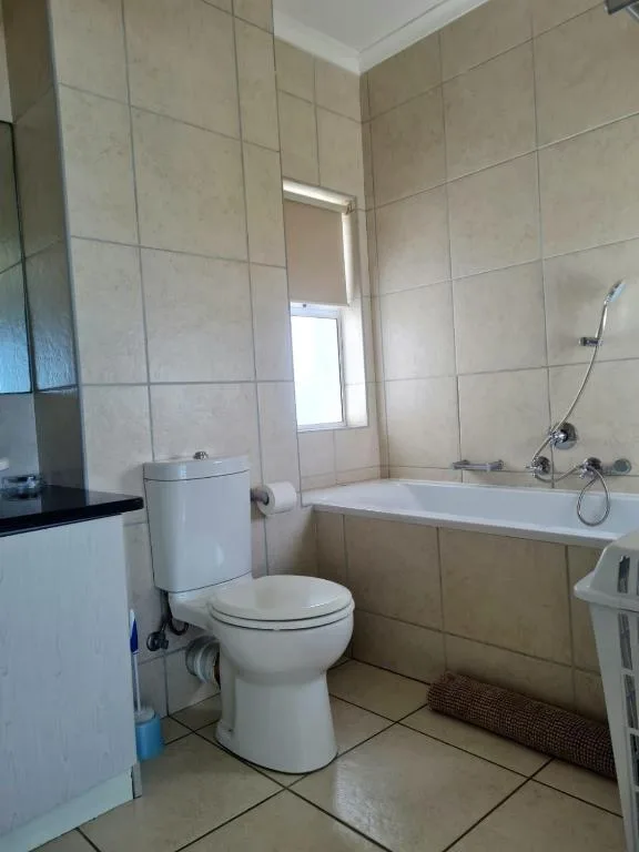 Bathroom with toilet, bathtub, and beige tile walls and flooring