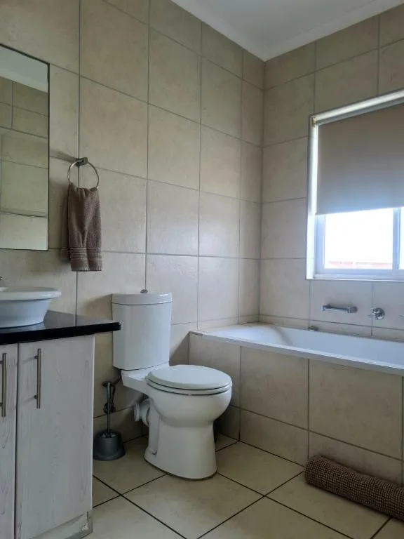 Clean bathroom with toilet, vanity, bathtub and tiled walls