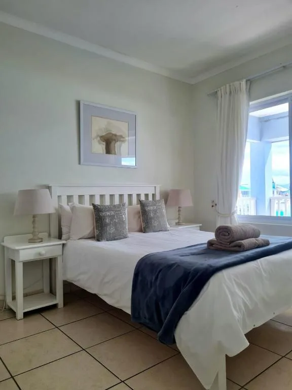 Bright bedroom with white bed, side tables, and ocean view through glass doors