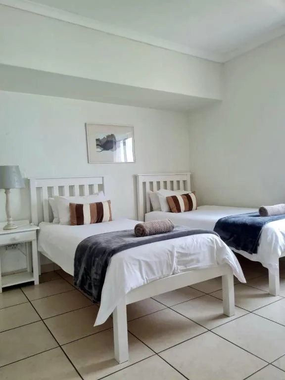 Twin bedroom with white wooden beds, striped cushions, and dark throws