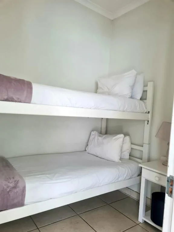 Clean bunk bed with white linens and purple accents in bright room
