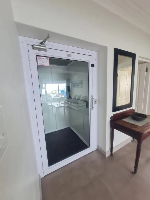 Modern glass elevator entrance with white frame and interior visibility