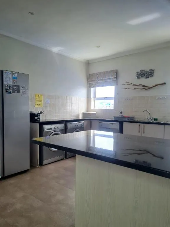 Spacious modern kitchen with black countertops, stainless steel appliances, and natural light
