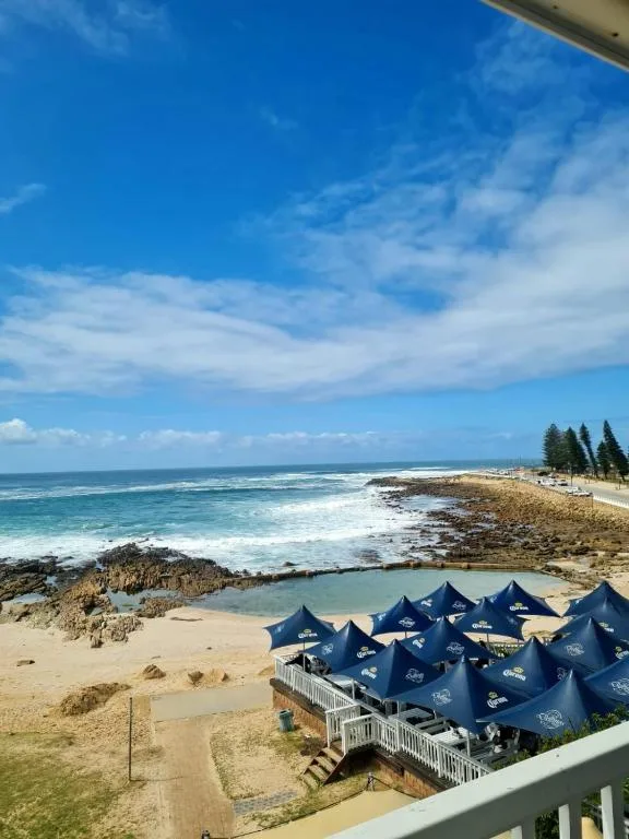 Coastal beach view with ocean, rocky shores, and blue umbrellas below