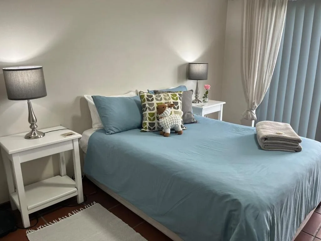 Bright bedroom with blue bedding, white nightstands, and soft lighting