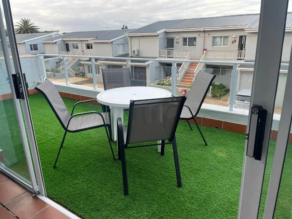 Outdoor patio with artificial grass, white table, and black chairs overlooking neighboring units