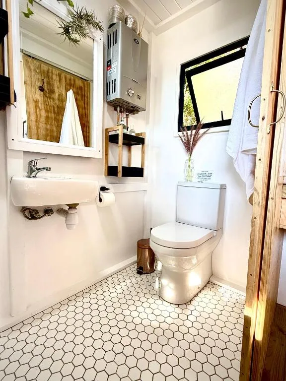 Bright bathroom with white toilet, sink, mirror, and hexagonal tile flooring