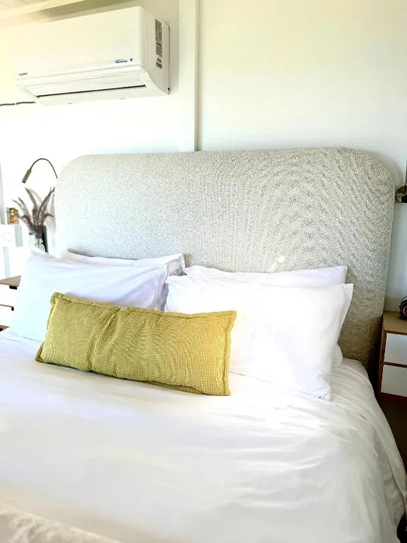 Bed with cream headboard, white linens, and yellow accent pillow