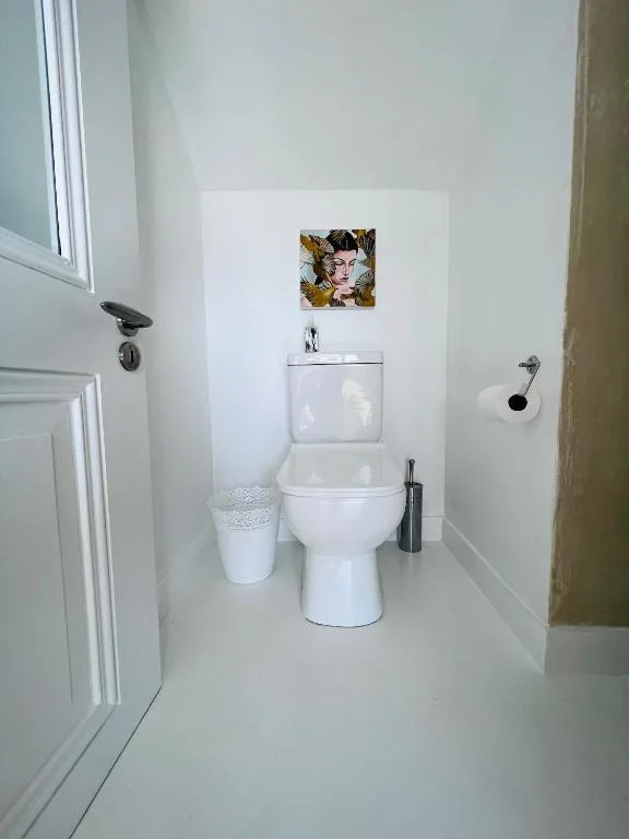 Clean white bathroom with toilet, small sink, and decorative wall art