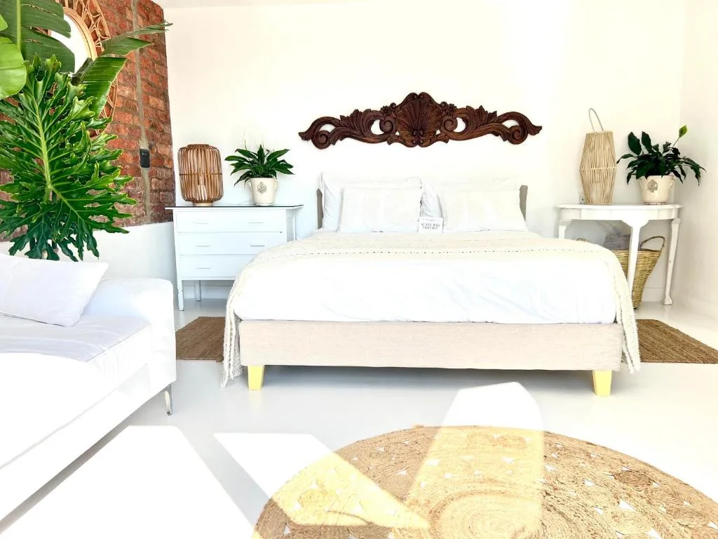 Bright bedroom with queen bed, white linens, potted plants, and exposed brick wall