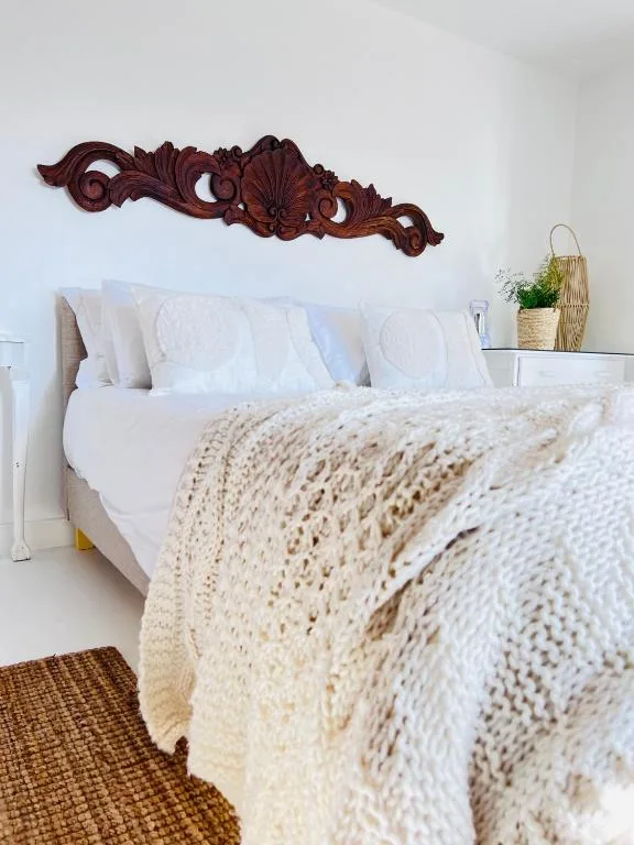 Bright bedroom with white pillows, cream knit throw, wooden wall art