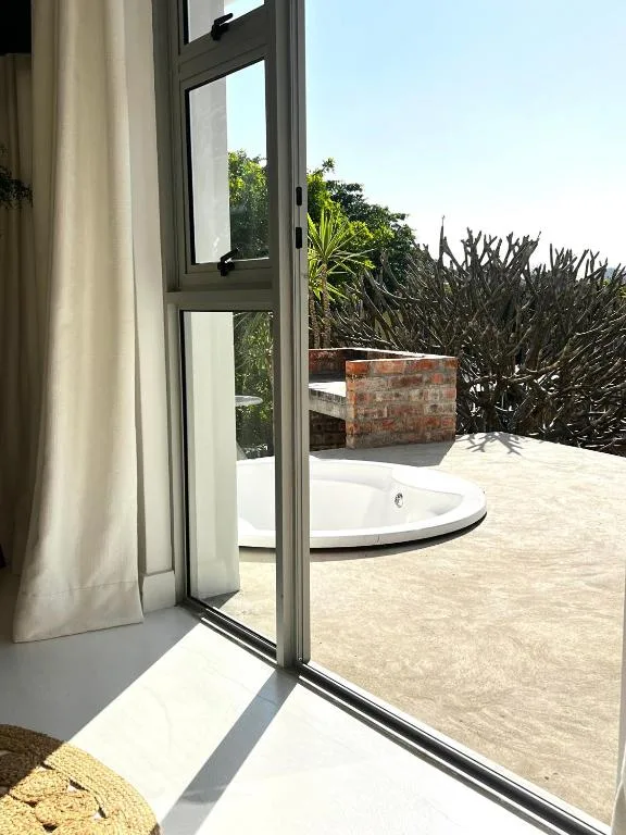 Open sliding doors leading to sunny patio with hot tub and garden views