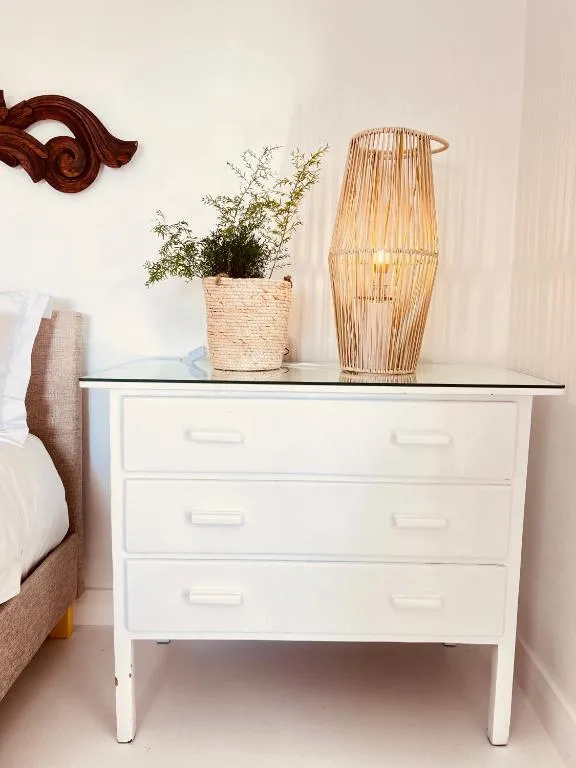 White bedside table with potted plant and woven lamp decor