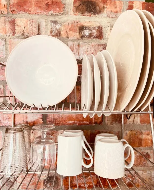 Kitchen shelving displaying white plates, bowls, and ceramic mugs against rustic brick