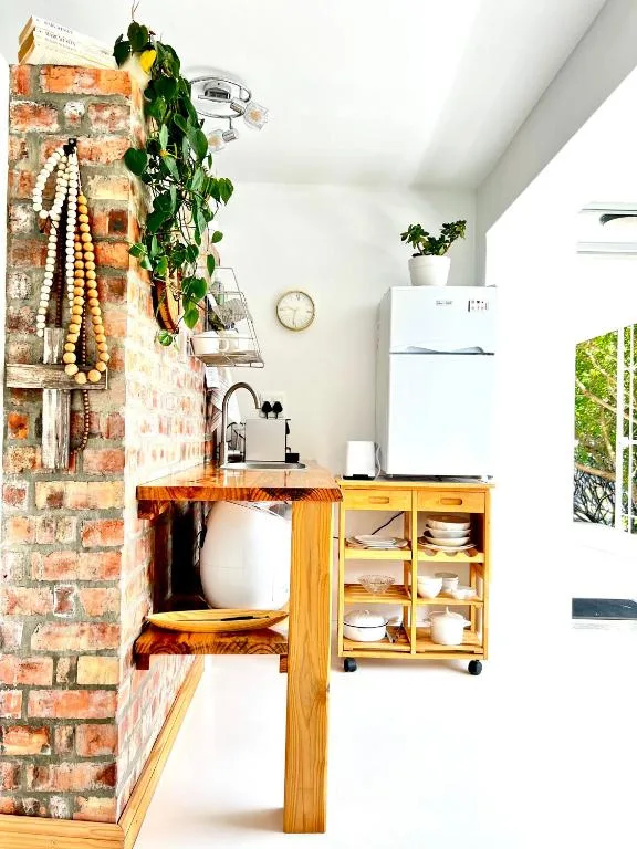 Compact kitchen with wooden cabinetry, white fridge, and exposed brick accent wall