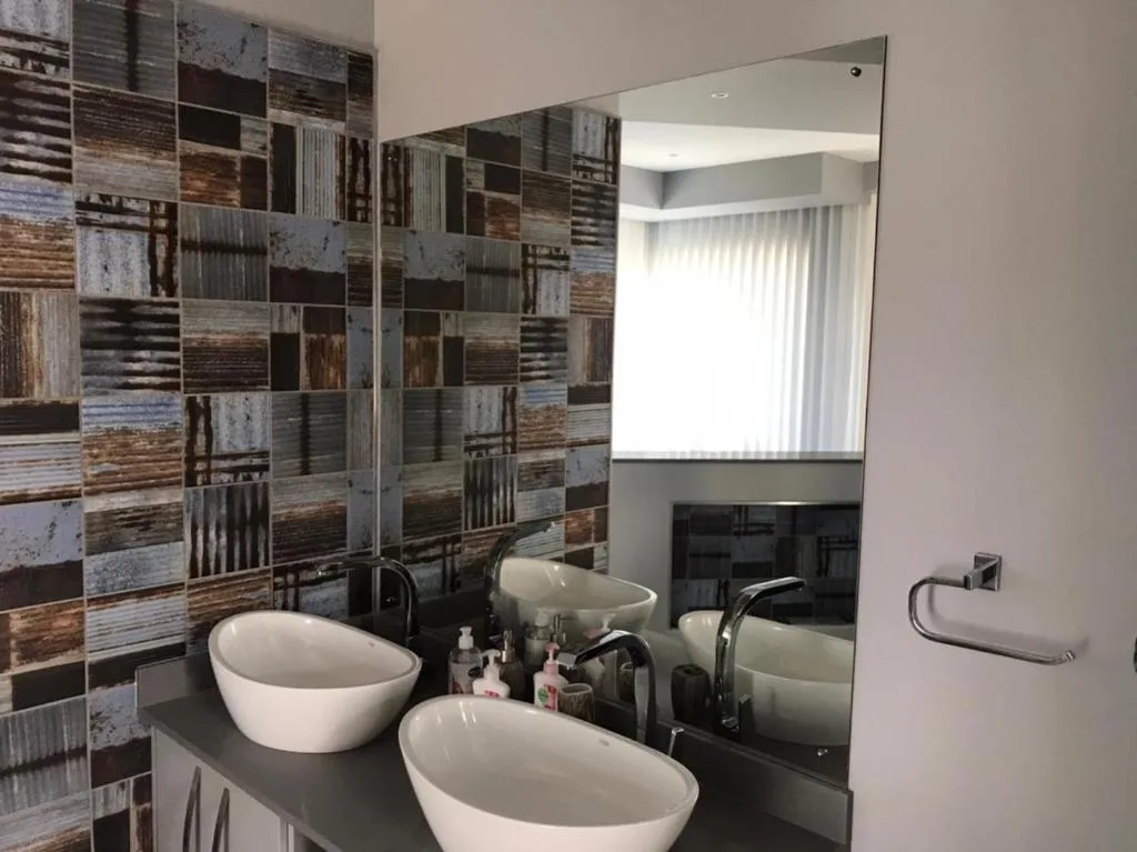 Modern bathroom with dual vessel sinks, large mirror, and textured tile wall
