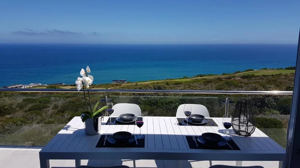 Outdoor dining table on cliffside deck overlooking turquoise ocean