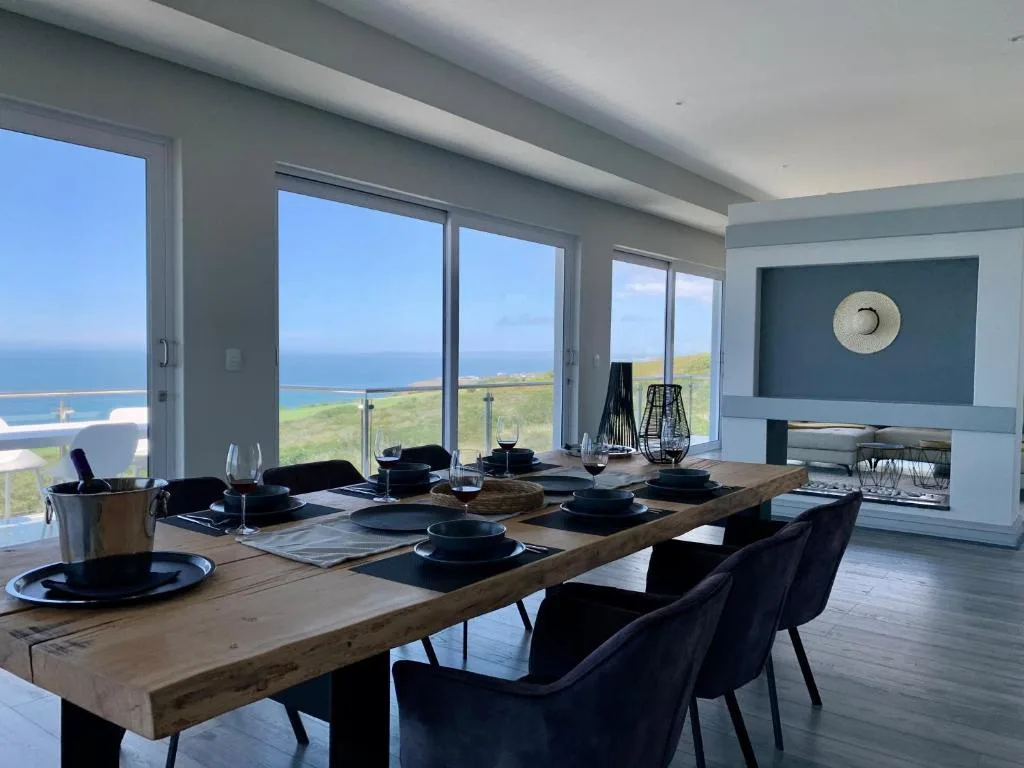 Modern dining room with ocean and coastal landscape views through floor-to-ceiling windows
