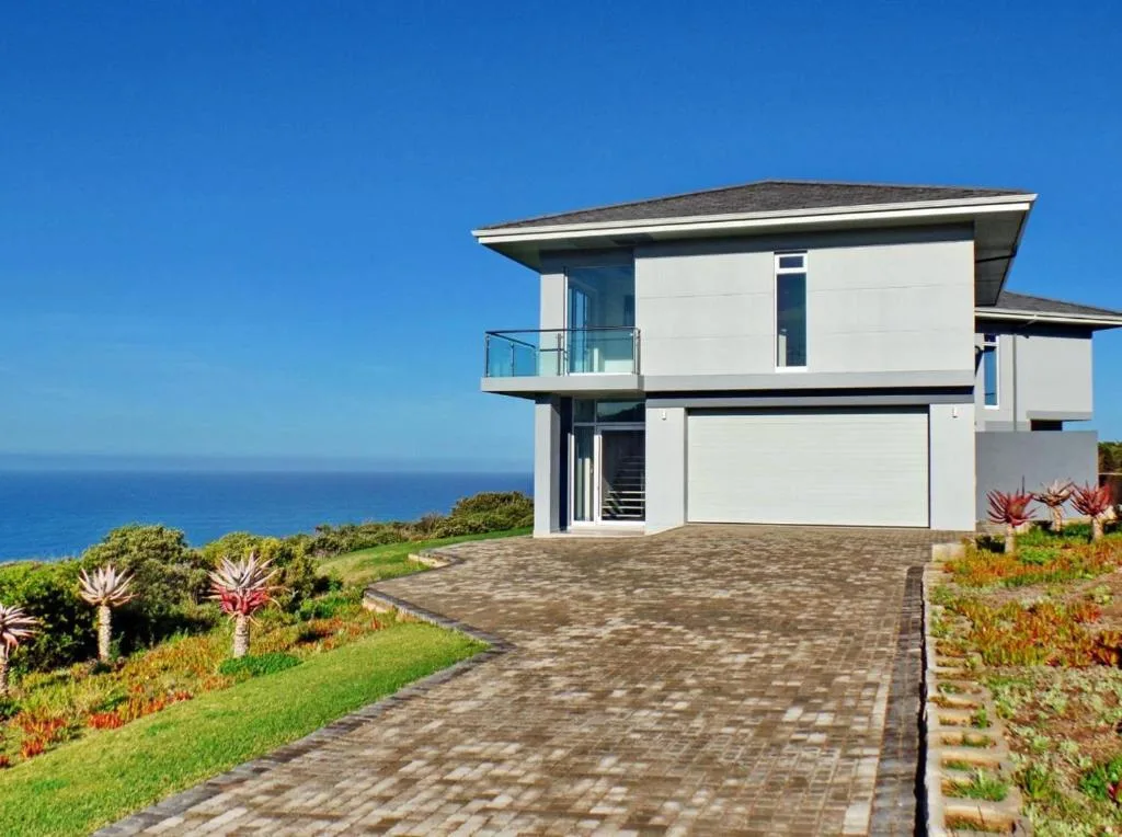 Modern white villa with ocean view, paved driveway, and coastal garden landscaping