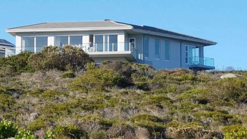 Modern blue and white villa perched on rocky coastal hillside with vegetation