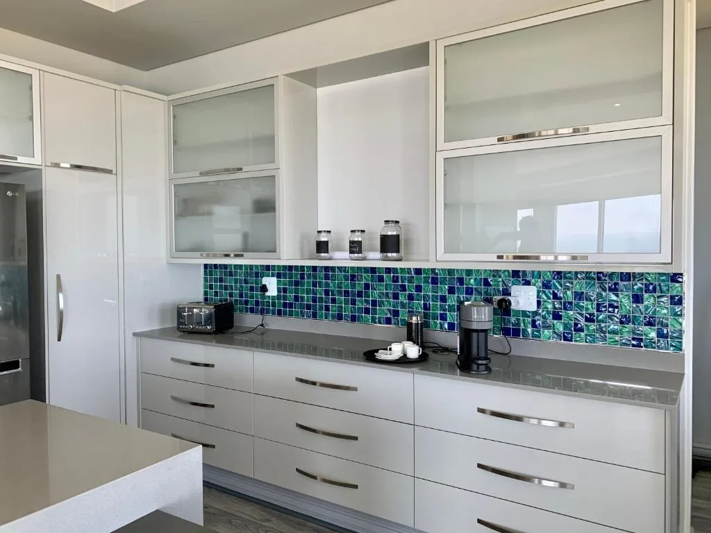 Modern kitchen with white cabinetry, green tile backsplash, and gray countertops