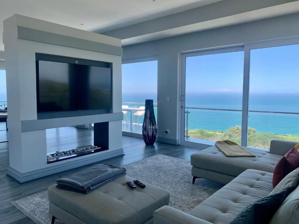 Modern lounge with fireplace, TV, seating, ocean views through glass doors