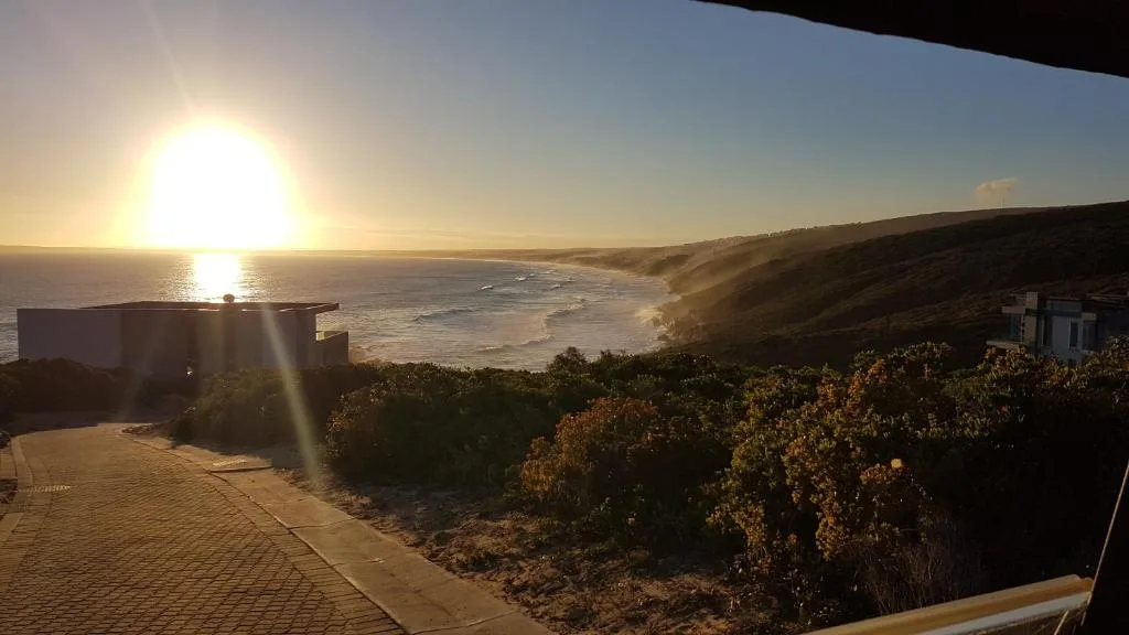 Sunrise over ocean and beach with coastal cliffs, viewed from property deck