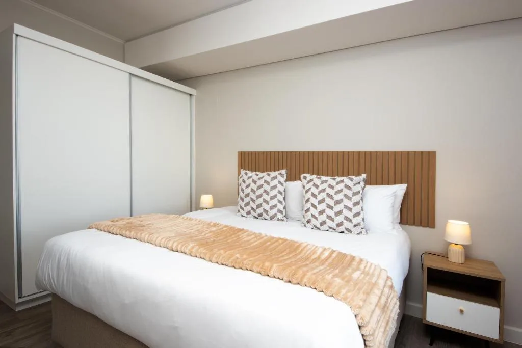 Modern bedroom with white bedding, patterned pillows, wood headboard, and side tables