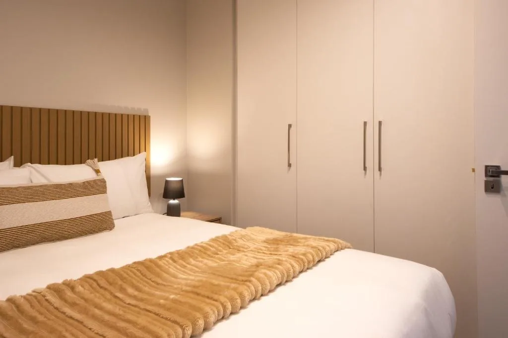 Modern bedroom with textured headboard, white bedding, and built-in wardrobe storage