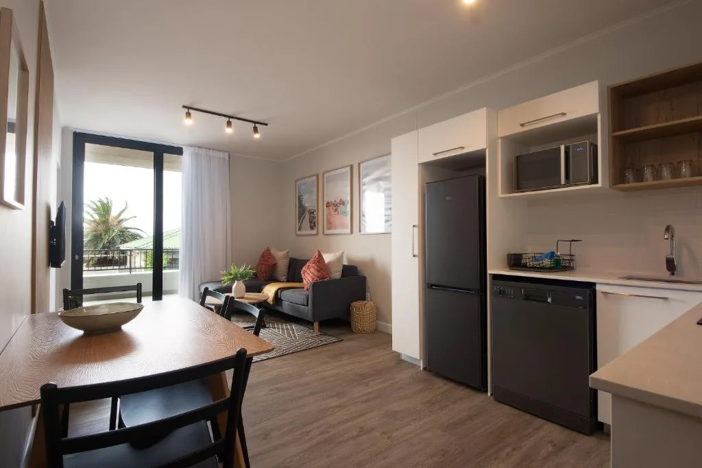 Open-plan lounge with black sofa, dining table, and kitchen area visible