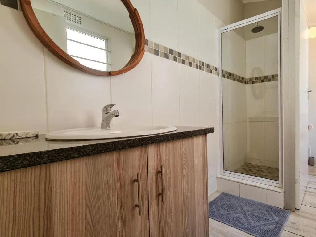 Modern bathroom with wooden vanity, round mirror, and glass shower enclosure