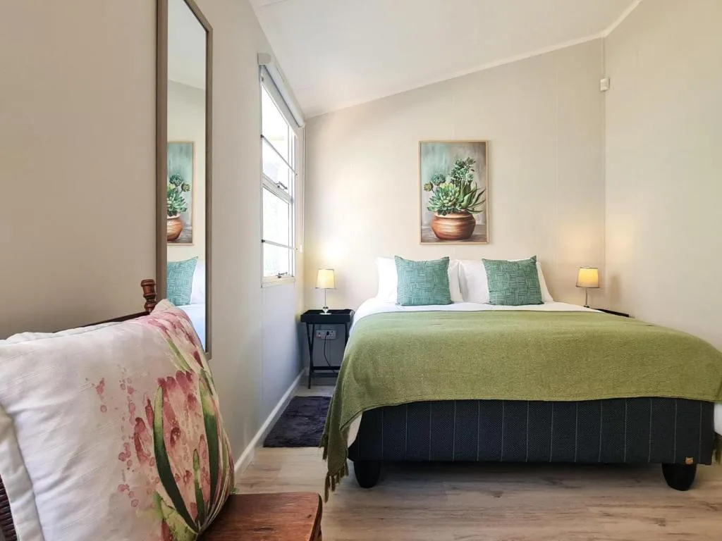 Bright bedroom with green bedspread, turquoise pillows, and succulent artwork