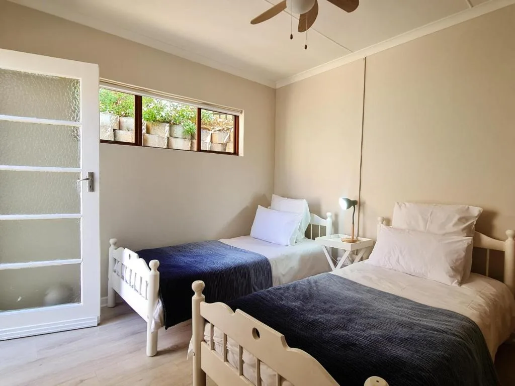 Twin bedroom with white frames, dark bedding, and ceiling fan