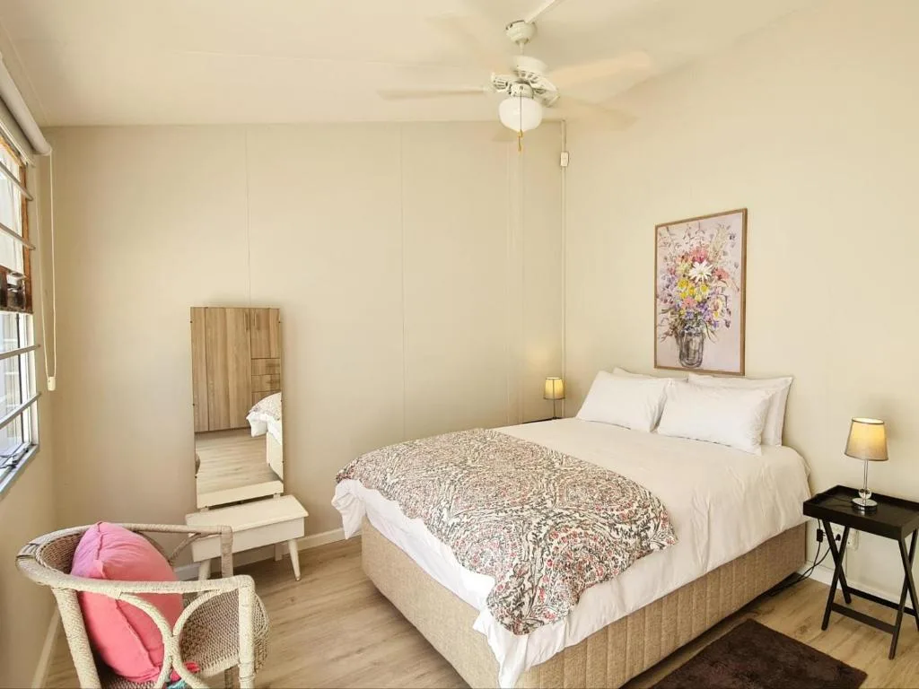 Bright bedroom with double bed, floral artwork, and wicker chair with pink cushion
