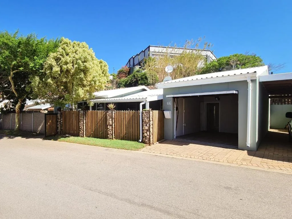 Modern white holiday home with wooden gate and paved driveway, garden surrounds